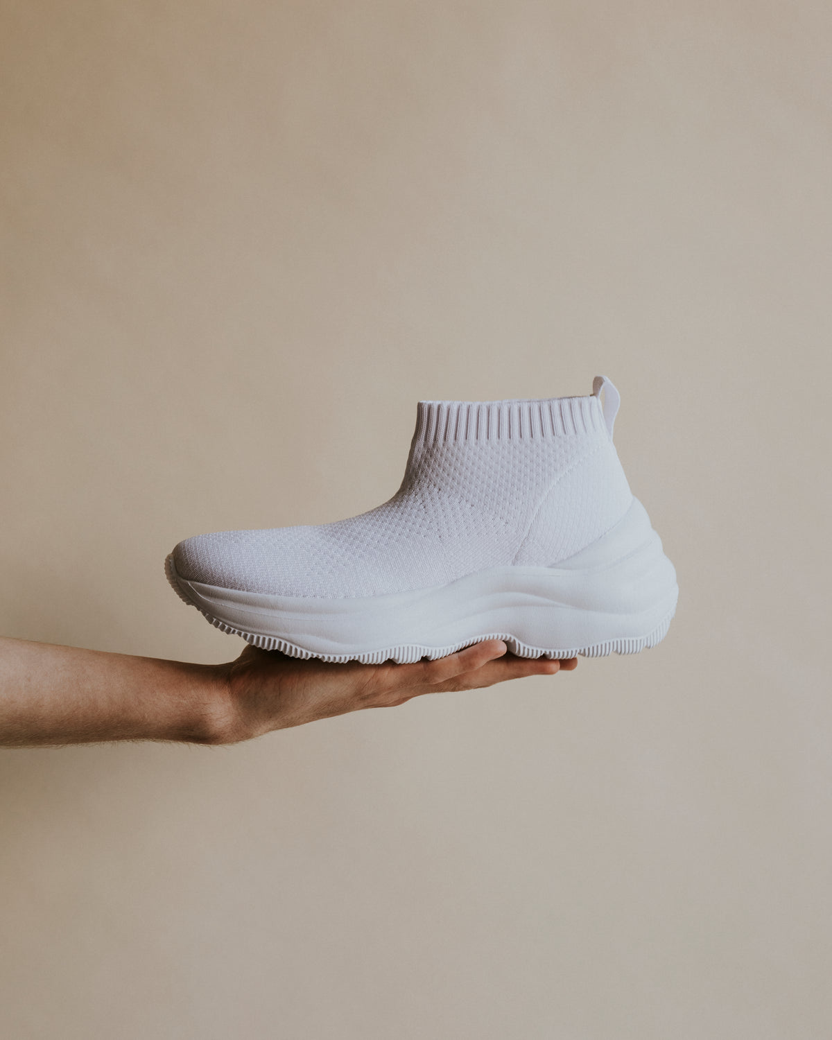 White sneaker held in hand on beige background